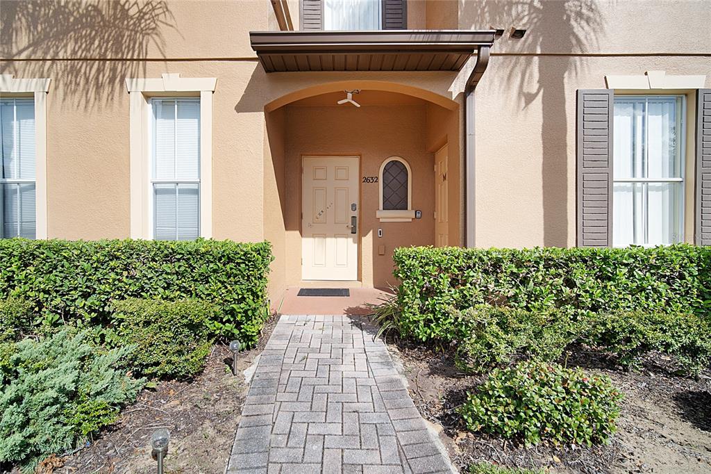 A paved walkway leads to the front entrance of a tan house with green hedges — 2632 CALABRIA AVENUE, DAVENPORT, FL