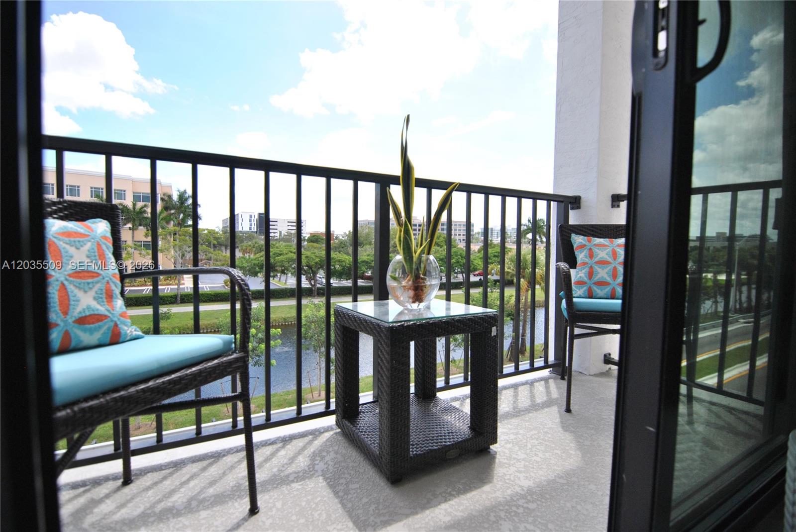 A balcony features two wicker chairs with patterned pillows, a side table, and water views — 8301 NW 41st # 302, Doral FL 33166, DORAL, FL