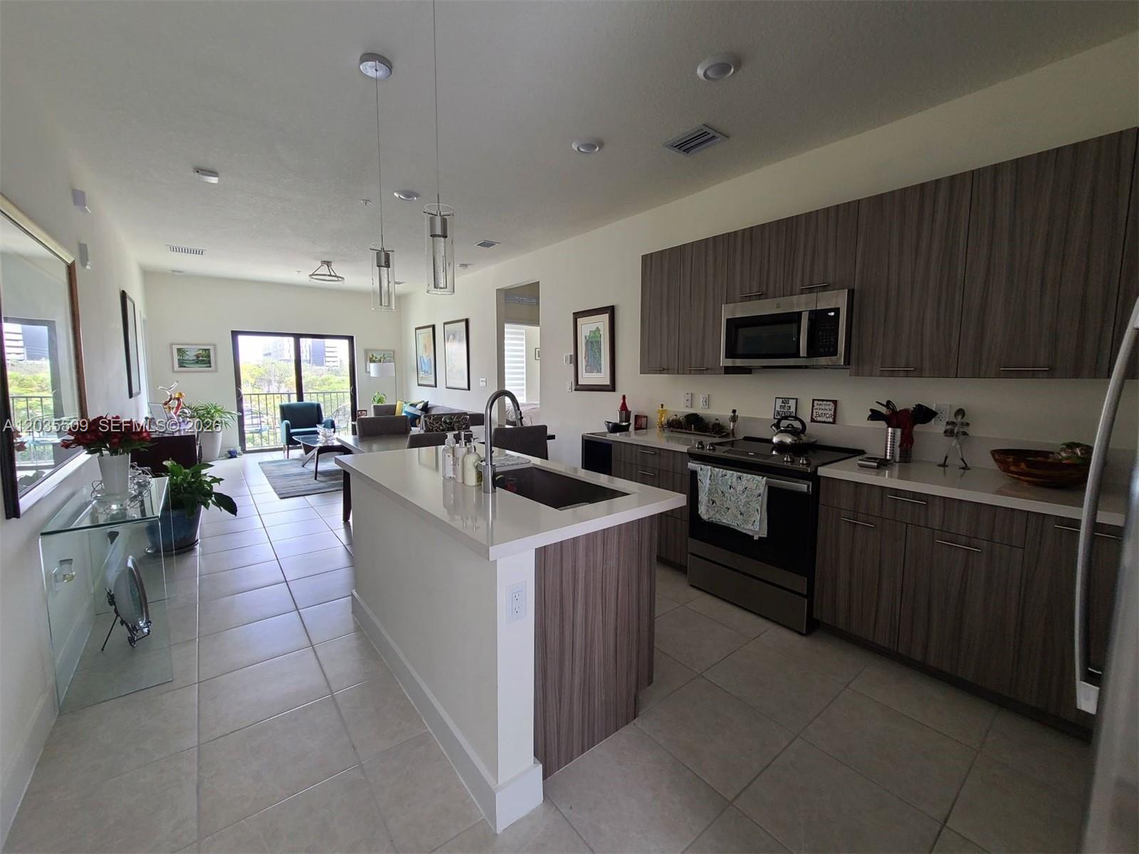 A modern kitchen with wood-toned cabinets and a white island opens into a living area — 8301 NW 41st # 302, Doral FL 33166, DORAL, FL