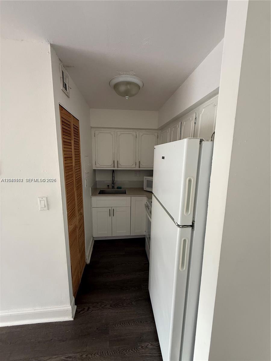 This small kitchen features white cabinets, a white refrigerator, and dark wood-look flooring — 5199 NW 7th St # 111, Miami FL 33126, MIAMI, FL