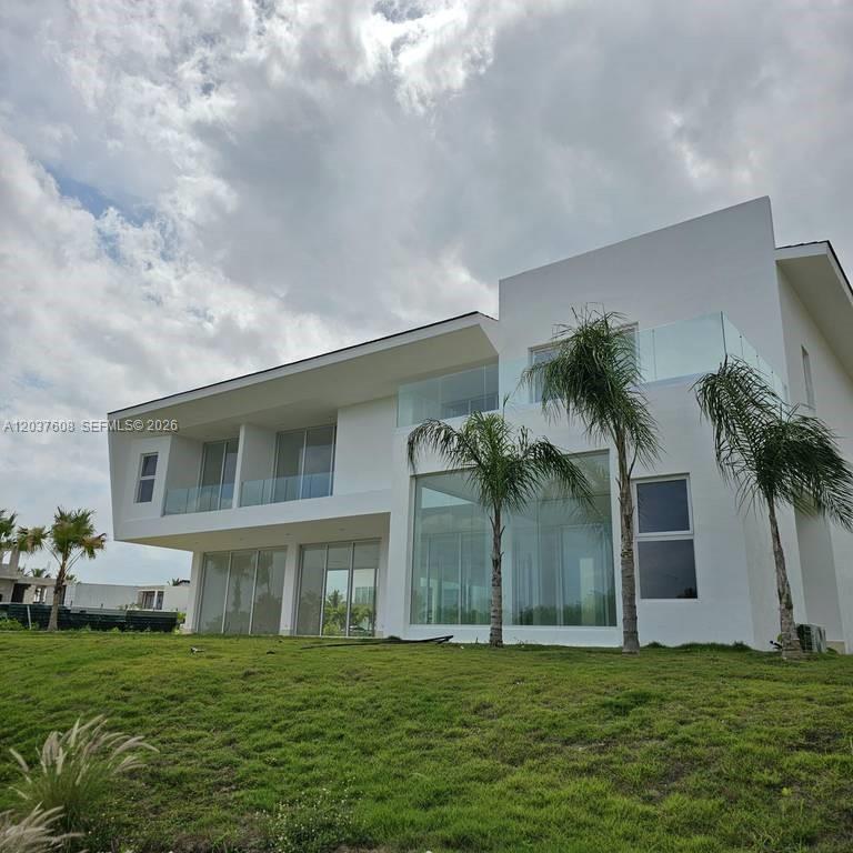 A modern two-story white house features large glass windows, balconies with glass railings, and palm trees — 0 Cap Cana., FL