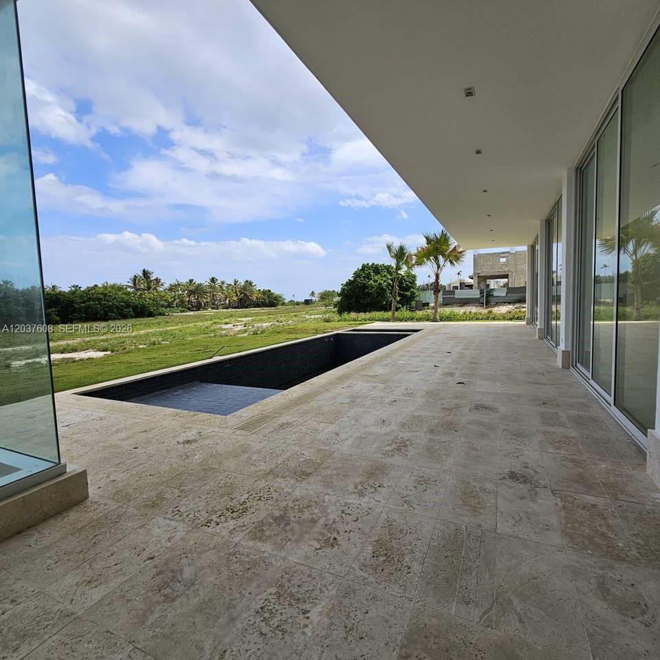 A modern patio with travertine flooring overlooks a rectangular swimming pool and a grassy field — 0 Cap Cana., FL