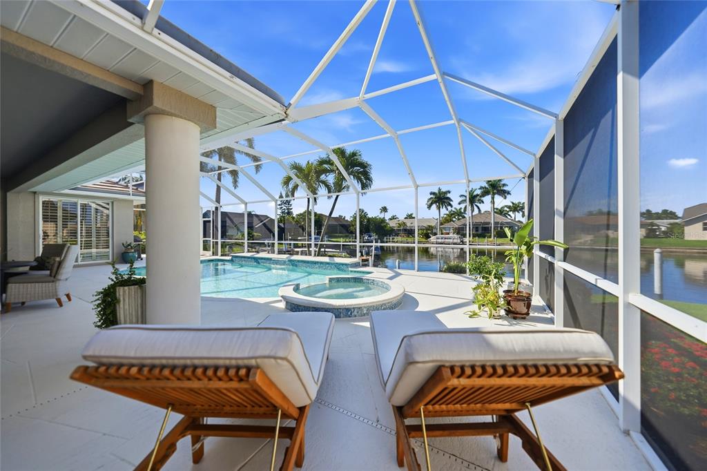 A screened-in pool deck features two lounge chairs, a spa, and a view of water — 523 SAINT GIRONS COURT, PUNTA GORDA, FL
