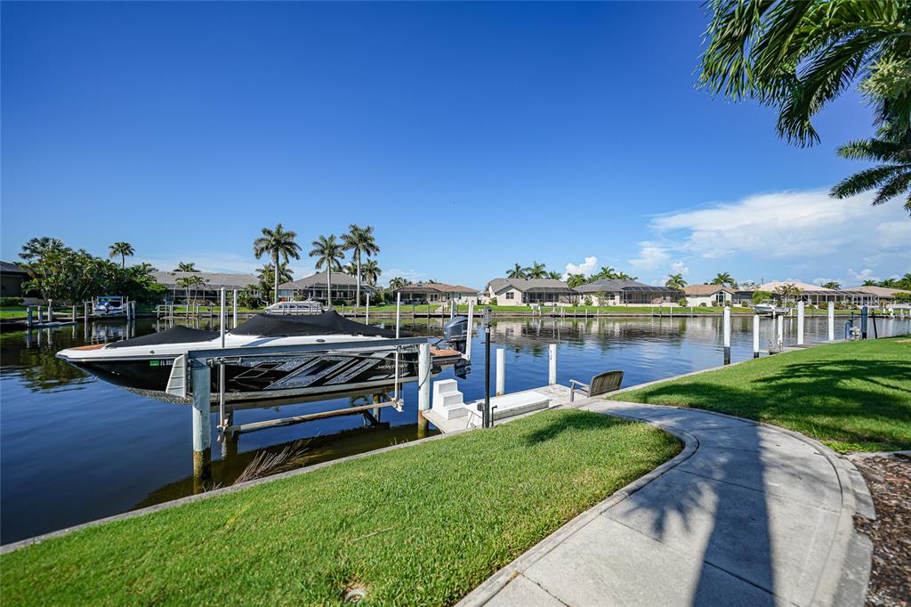 A boat sits on a lift in a canal behind a grassy backyard with palm trees — 523 SAINT GIRONS COURT, PUNTA GORDA, FL
