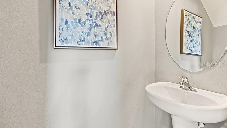 A powder room features a pedestal sink, a round mirror, and abstract wall art — 4029 GOLD DUST LANE, SARASOTA, FL