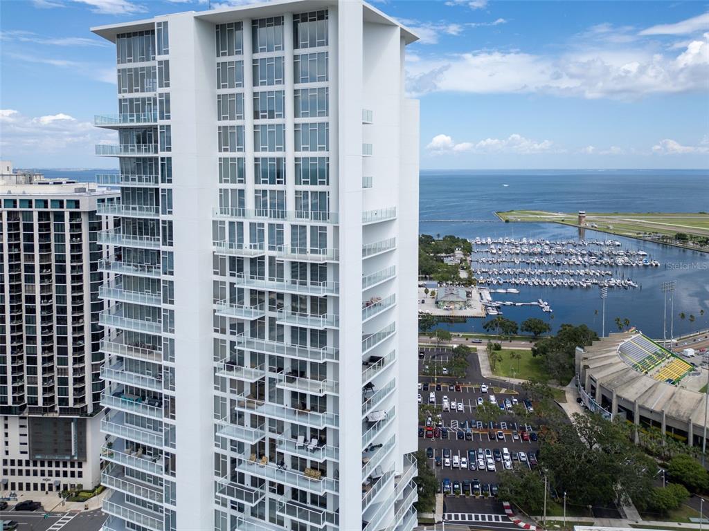 An aerial view shows a tall white residential tower next to a marina and stadium — 175 1ST STREET S UNIT 905, ST PETERSBURG, FL