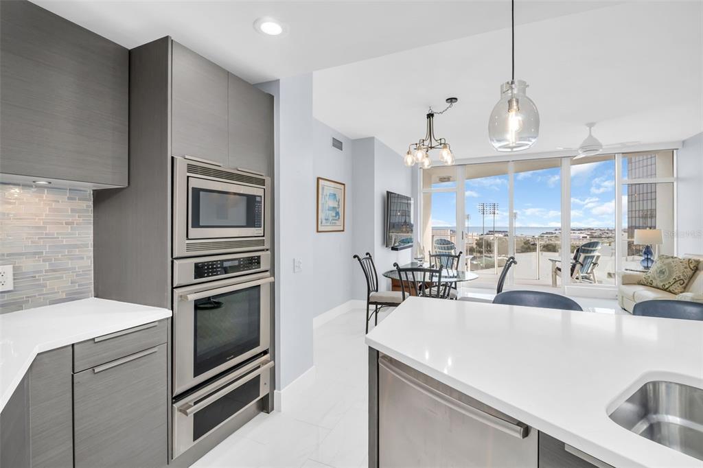 A modern kitchen with grey cabinetry and stainless steel appliances overlooks a dining area and balcony — 175 1ST STREET S UNIT 905, ST PETERSBURG, FL