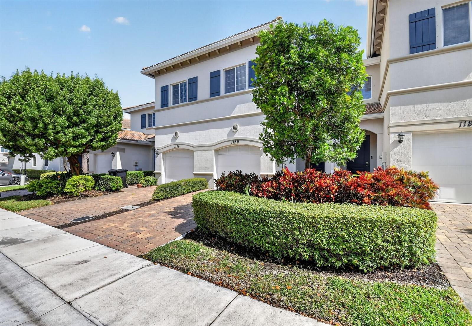 A two-story townhouse exterior features a brick driveway, manicured hedges, and a small tree — 1186 Paisley Court, FL 33461, FL