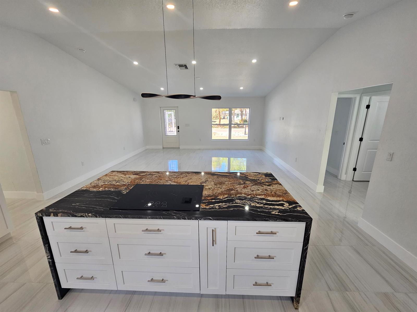 A kitchen island with a dark granite countertop and white cabinets sits in an open room — 2964 NW 36th Avenue, Okeechobee FL 34972, OKEECHOBEE, FL