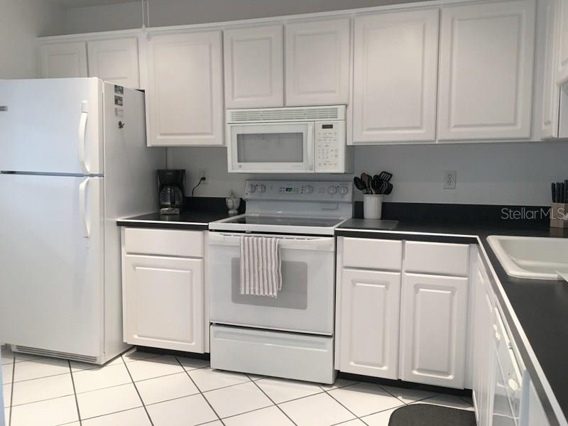 A kitchen with white cabinets, black countertops, white appliances, and white tiled flooring — 3660 IRONWOOD CIRCLE UNIT 503M, BRADENTON, FL