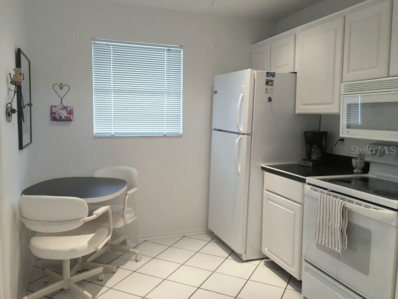 A kitchen features white cabinets, white appliances, a small dining table, and tiled flooring — 3660 IRONWOOD CIRCLE UNIT 503M, BRADENTON, FL