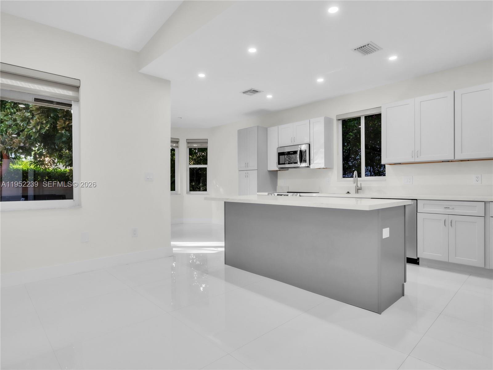 A modern kitchen features white cabinets, a gray island, and glossy white tile flooring — 12608 SW 121st Ave, Miami FL 33186, MIAMI, FL