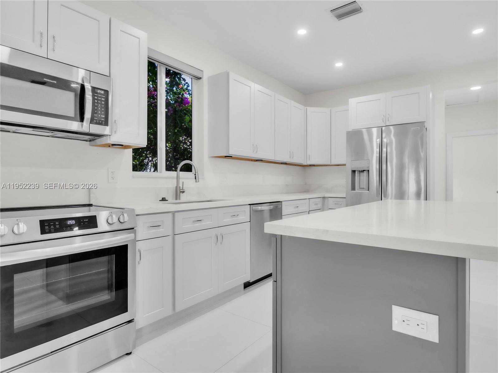 A modern kitchen features white cabinets, stainless steel appliances, and a gray kitchen island — 12608 SW 121st Ave, Miami FL 33186, MIAMI, FL