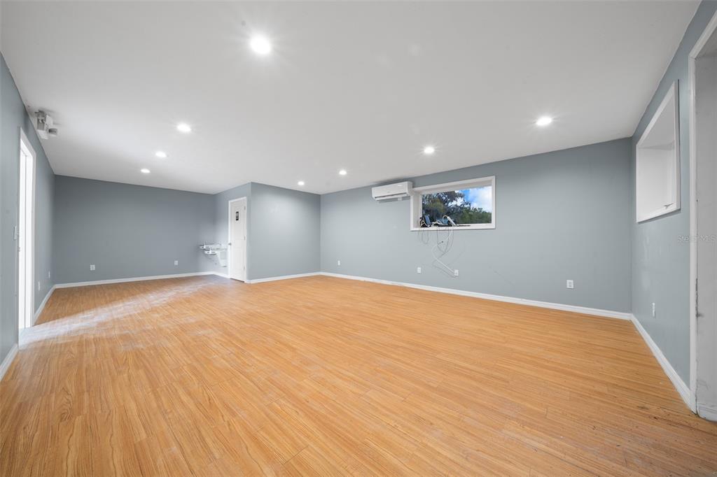 An empty room features light wood-look flooring, gray walls, recessed lighting, and a wall-mounted air conditioner — 3073 NE 37TH PLACE, WILDWOOD, FL