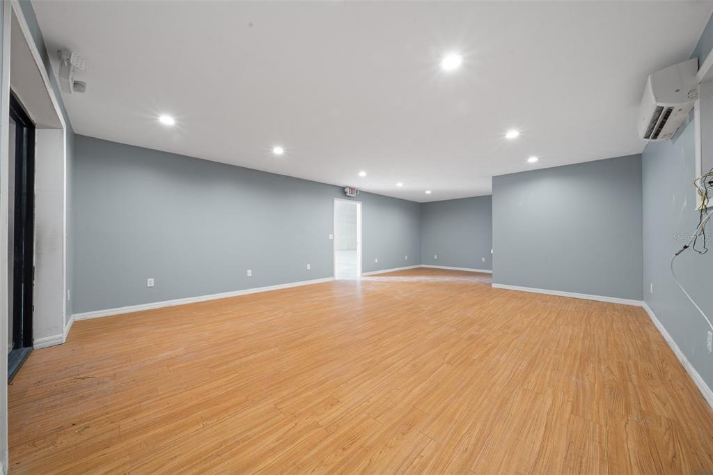 An empty room with light wood-look flooring, gray walls, recessed lighting, and a wall-mounted AC unit — 3073 NE 37TH PLACE, WILDWOOD, FL