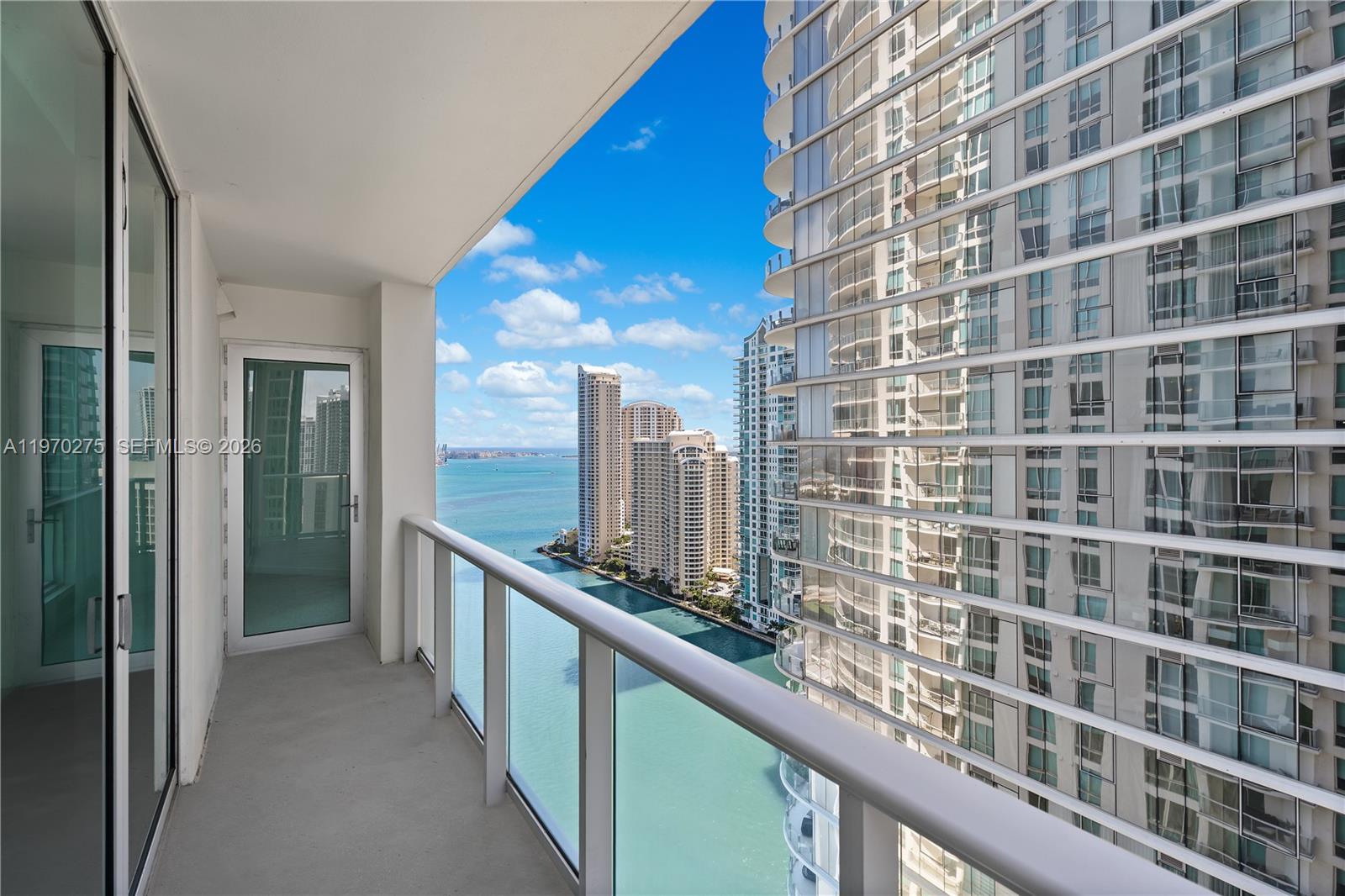 A high-rise balcony overlooks a bay and neighboring skyscrapers under a blue sky — 300 S Biscayne Blvd # 2602, Miami FL 33131, MIAMI, FL
