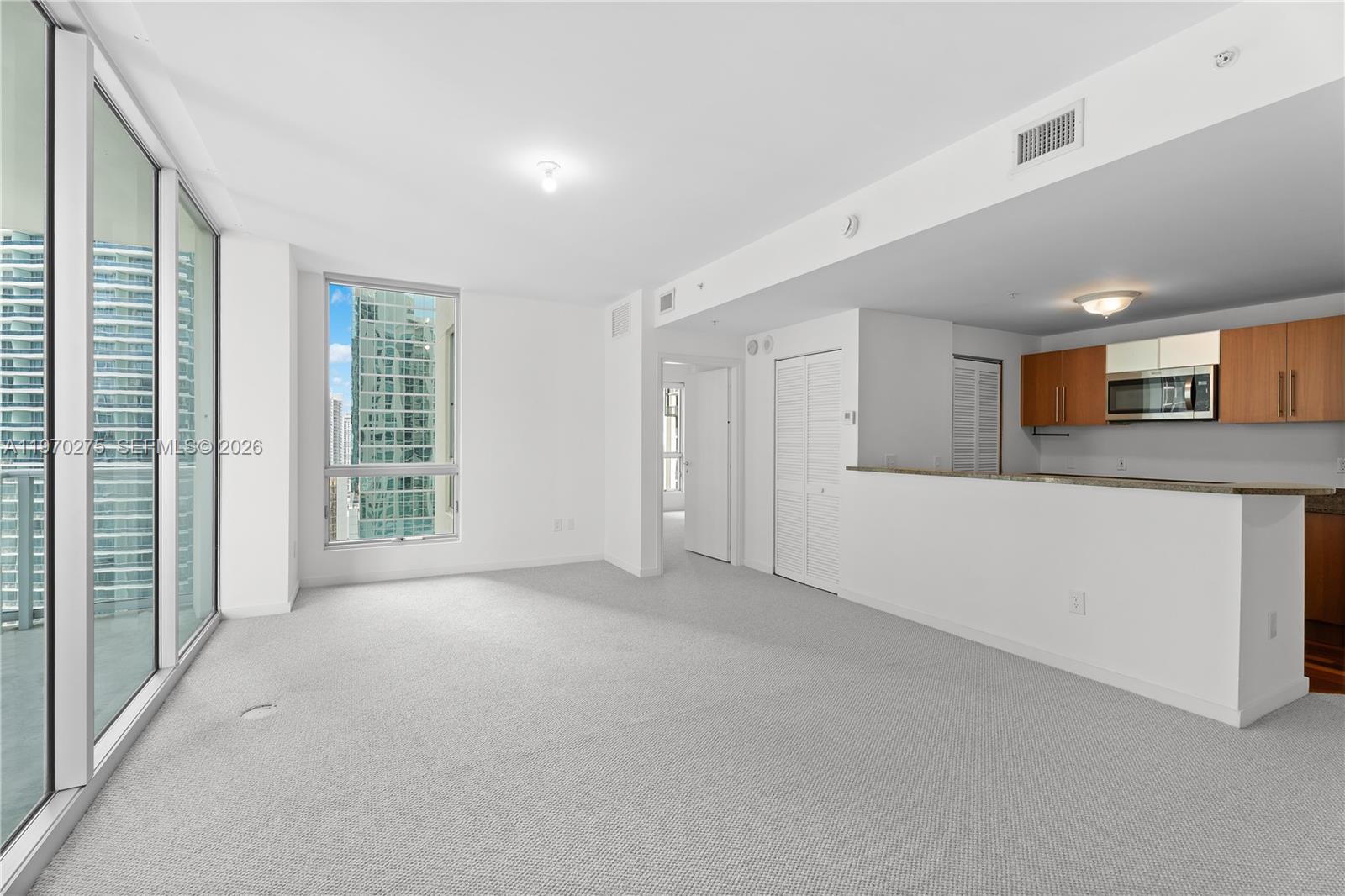 An open-concept living area features wall-to-wall carpeting, floor-to-ceiling windows, and an adjacent kitchen — 300 S Biscayne Blvd # 2602, Miami FL 33131, MIAMI, FL
