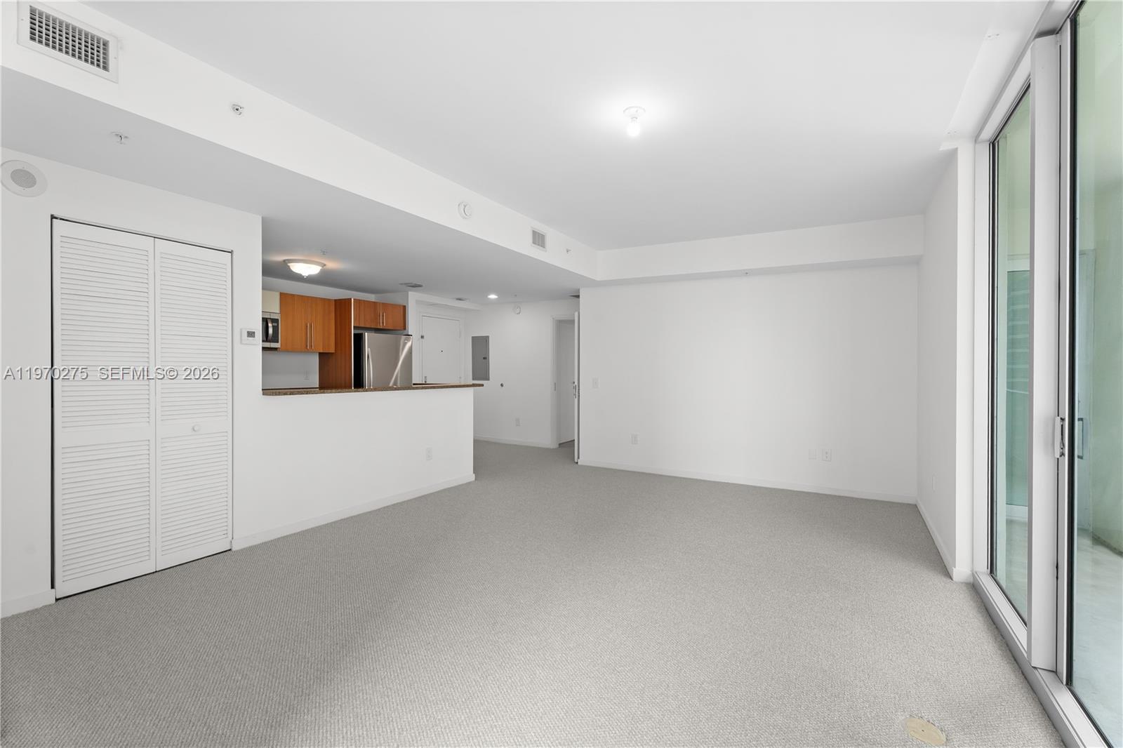 This living room features gray carpeting, white walls, and an open kitchen with wood cabinets — 300 S Biscayne Blvd # 2602, Miami FL 33131, MIAMI, FL