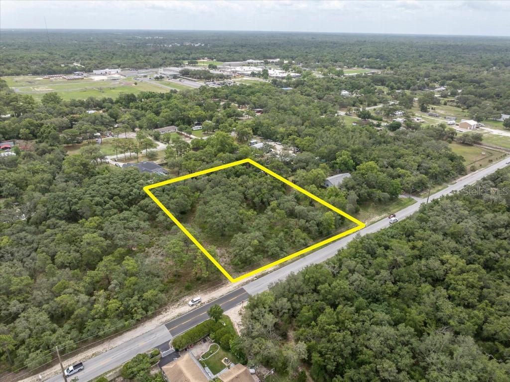 An aerial view shows a rectangular, tree-covered vacant lot outlined in yellow along a road — 0 HICKS ROAD, HUDSON, FL