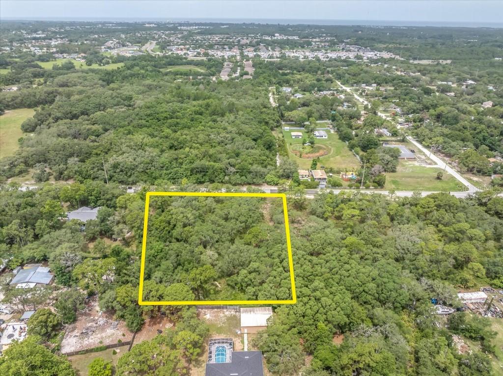 An aerial view shows a rectangular, tree-covered vacant lot outlined in yellow — 0 HICKS ROAD, HUDSON, FL