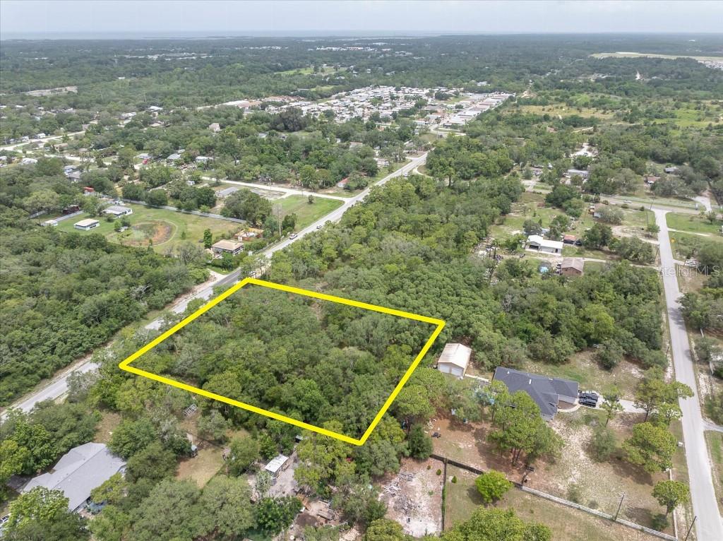 An aerial view shows a rectangular, tree-covered vacant lot outlined in yellow near a road — 0 HICKS ROAD, HUDSON, FL