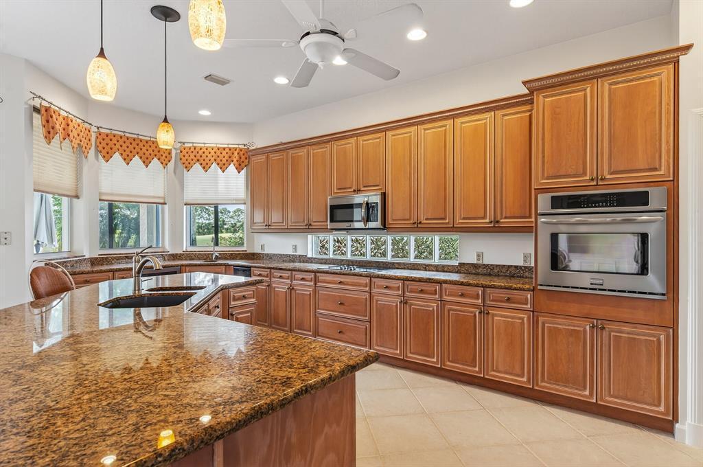 A kitchen features wood cabinets, granite countertops, stainless steel appliances, and a glass block backsplash — 3210 Bent Pine Drive, Fort Pierce FL 34951, FORT PIERCE, FL
