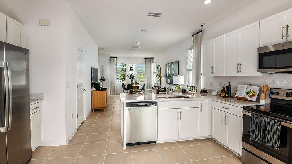 A modern kitchen with white cabinets and stainless steel appliances opens into a living area — 10609 ORBIT TERRACE, SARASOTA, FL