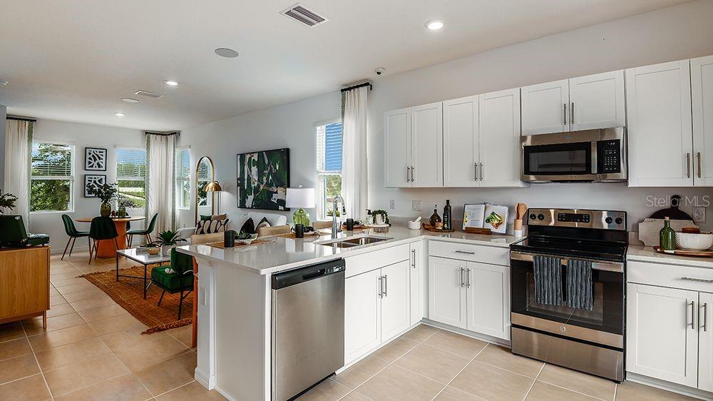 A modern kitchen with white cabinets and stainless steel appliances overlooks an open living area — 10609 ORBIT TERRACE, SARASOTA, FL