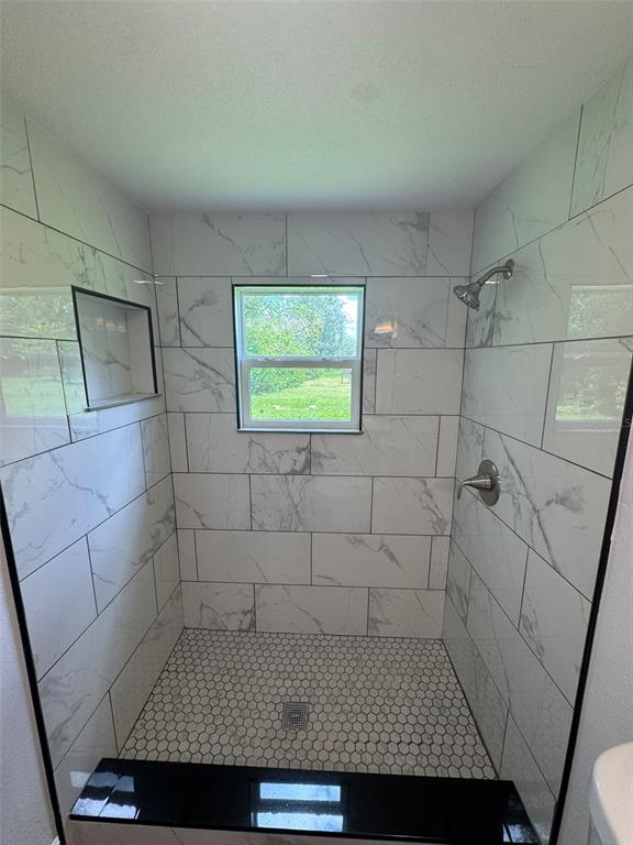 A walk-in shower features white marble-look wall tiles, a hexagonal floor, and a black bench — 904 ROBINSON AVENUE, ST CLOUD, FL