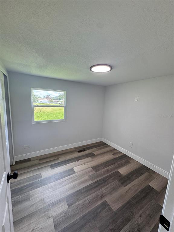 An empty bedroom features light gray walls, a single window, and wood-look plank flooring — 904 ROBINSON AVENUE, ST CLOUD, FL