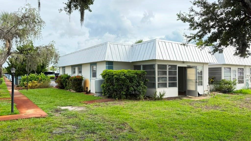 A single-story building with a white metal roof and screened-in porch sits on a lawn — 4248 TAMARGO DRIVE, NEW PORT RICHEY, FL