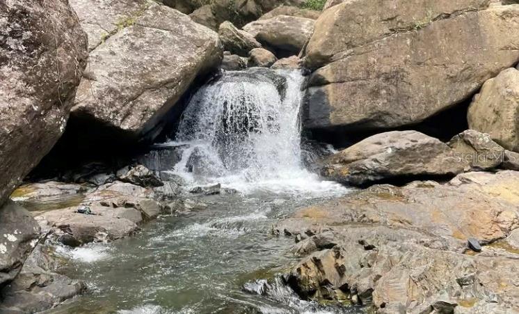 A small waterfall cascades over large rocks into a shallow stream — PR 956 KM 8.8 E SECTOR LOS MEDINAS BO GUZMAN ARRIBA, RIO GRANDE, PR