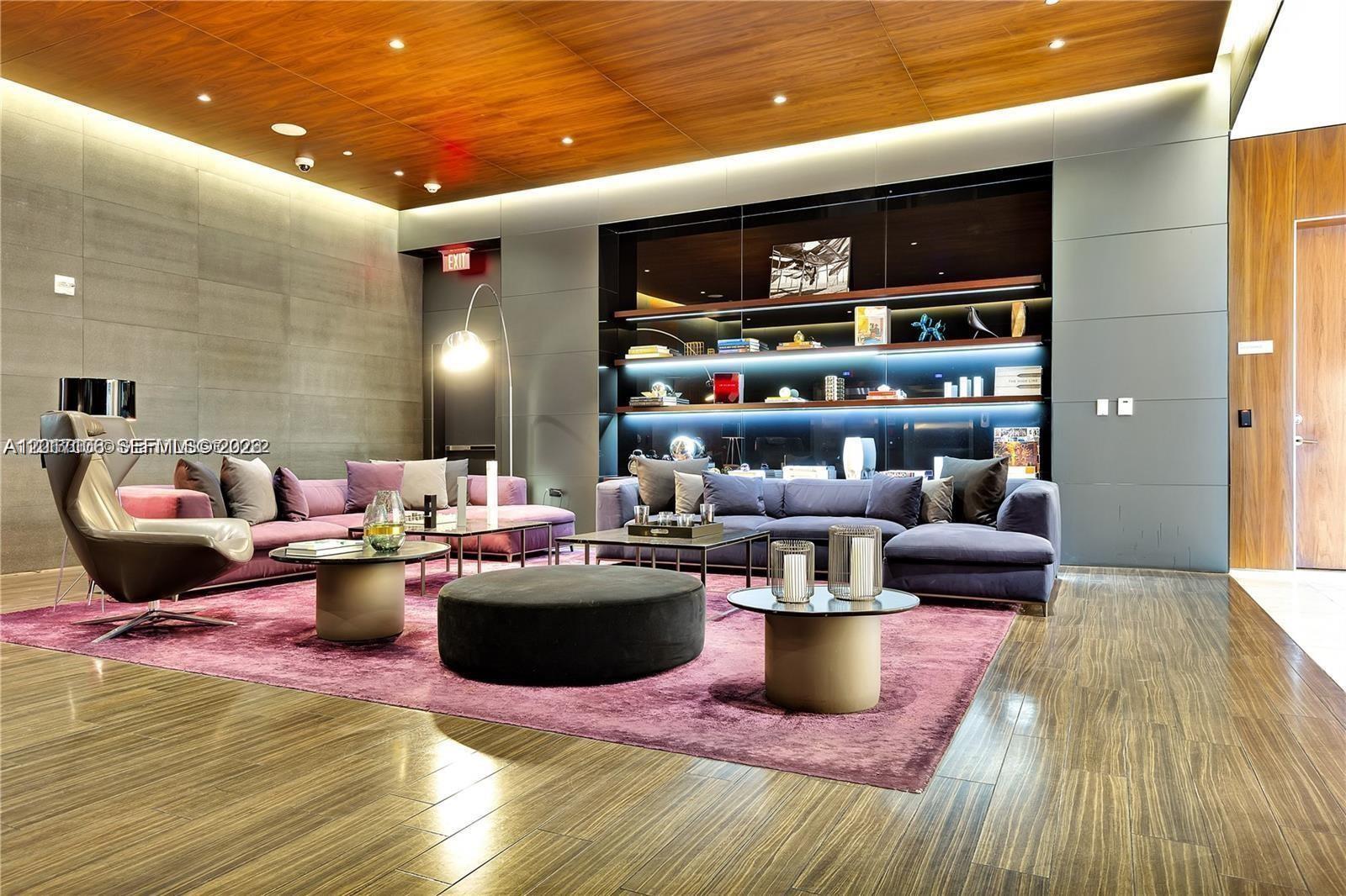 A modern lounge features a purple rug, two sofas, a swivel chair, and illuminated shelving — 68 SE 6th St # 2510, Miami FL 33131, MIAMI, FL