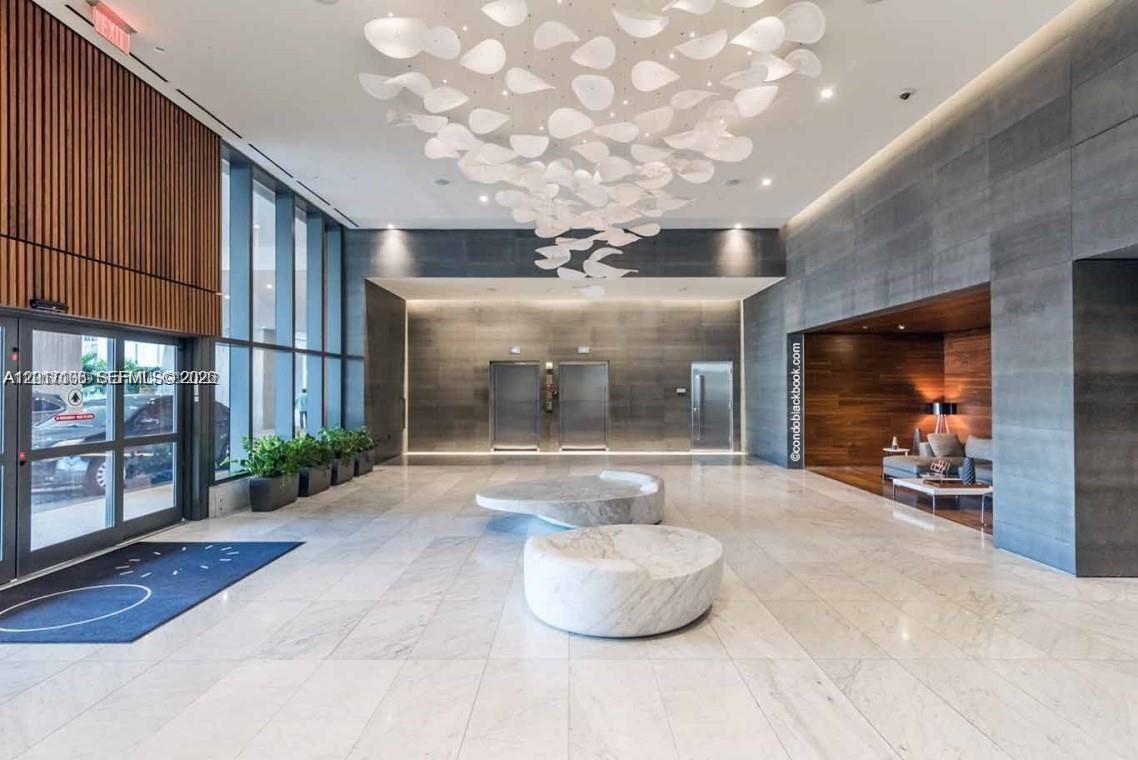 A modern building lobby features marble floors, two elevators, and a large sculptural ceiling light — 68 SE 6th St # 2510, Miami FL 33131, MIAMI, FL