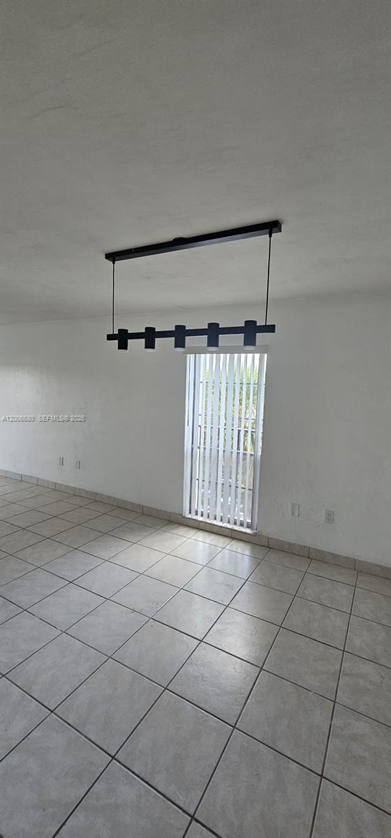 An empty room features white walls, light-colored tile flooring, and a modern black linear chandelier — 6884 N Kendall Dr # C404, Pinecrest FL 33156, PINECREST, FL