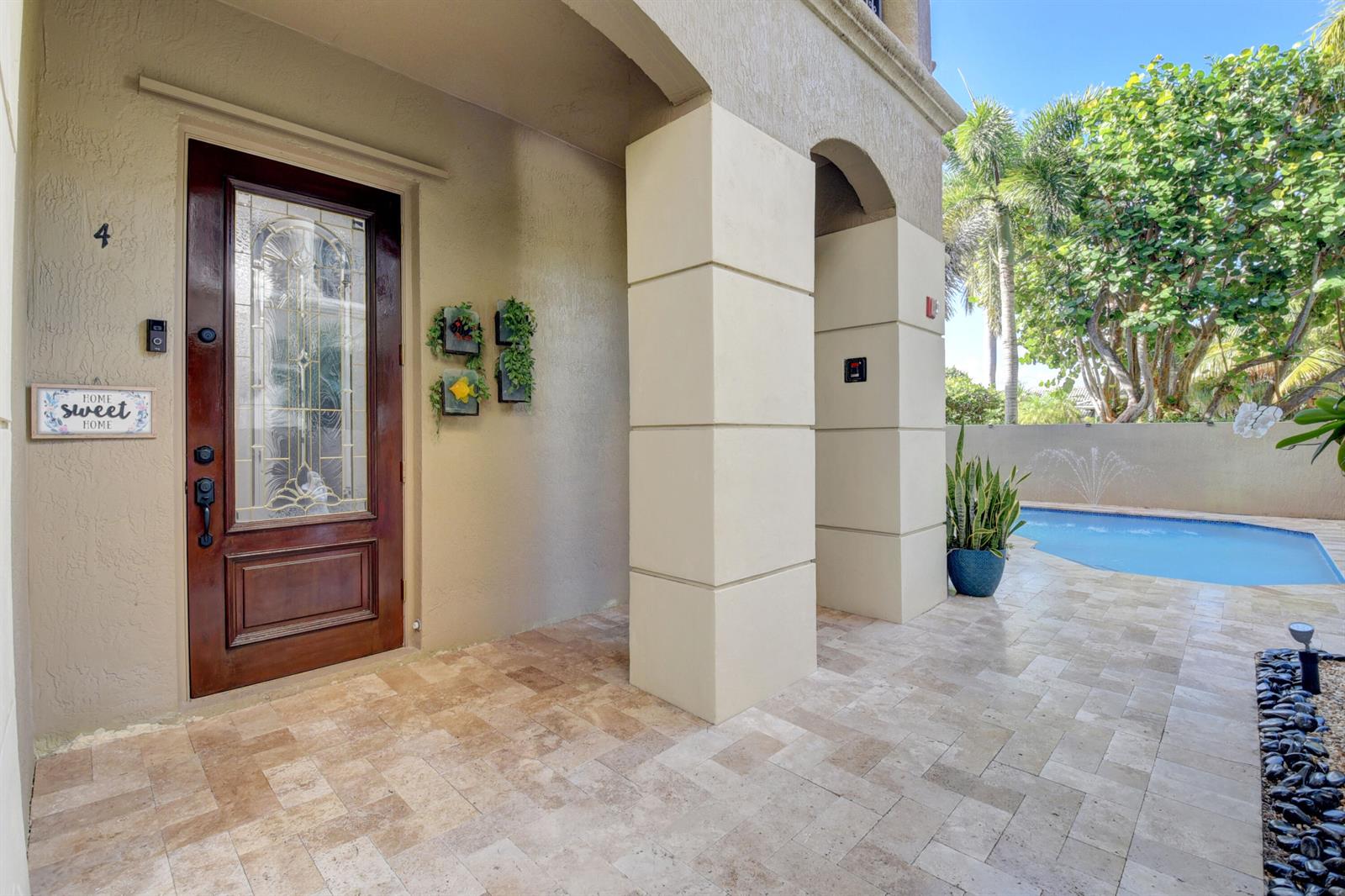 A covered entryway with a wooden door, stone pavers, and a view of a pool — 921 Osceola Drive Unit 4, Boca Raton FL 33432, BOCA RATON, FL