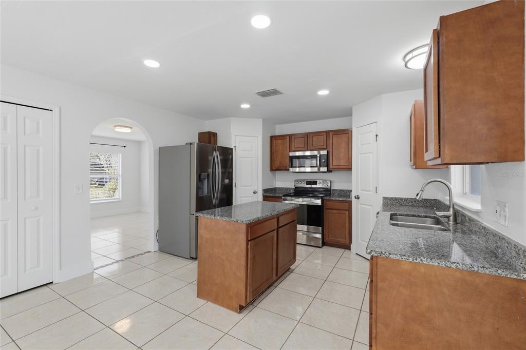 A kitchen with wood cabinets, granite countertops, stainless steel appliances, and a center island — 4140 STONEFIELD DRIVE, ORLANDO, FL