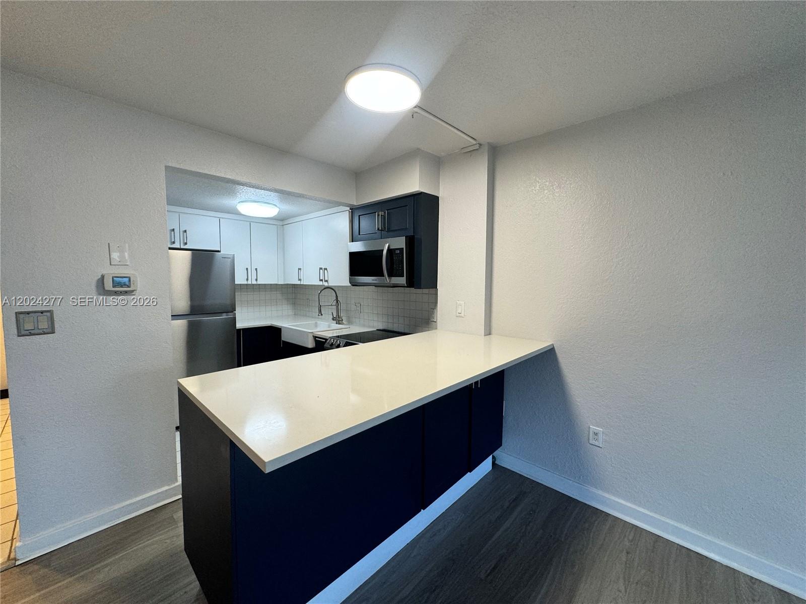 A kitchen features a white quartz breakfast bar, dark blue lower cabinets, and stainless appliances — 1650 NE 115th St # 609, Miami FL 33181, MIAMI, FL
