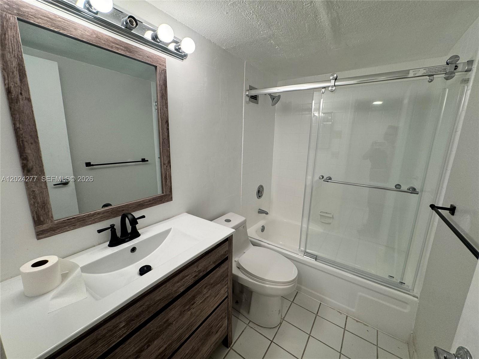 A bathroom features a wood-framed mirror, a white vanity, a toilet, and a glass-enclosed tub — 1650 NE 115th St # 609, Miami FL 33181, MIAMI, FL