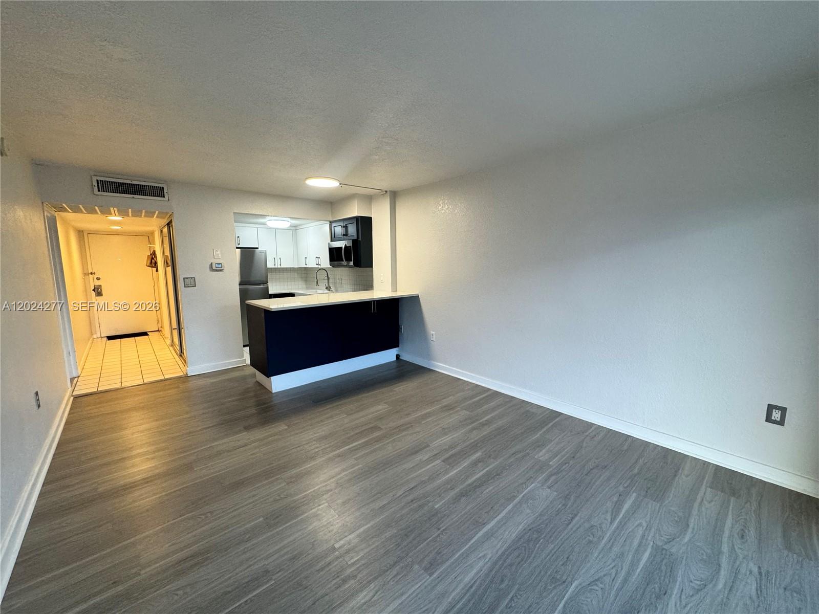 An open living area features gray wood-look flooring and a kitchen with a breakfast bar — 1650 NE 115th St # 609, Miami FL 33181, MIAMI, FL