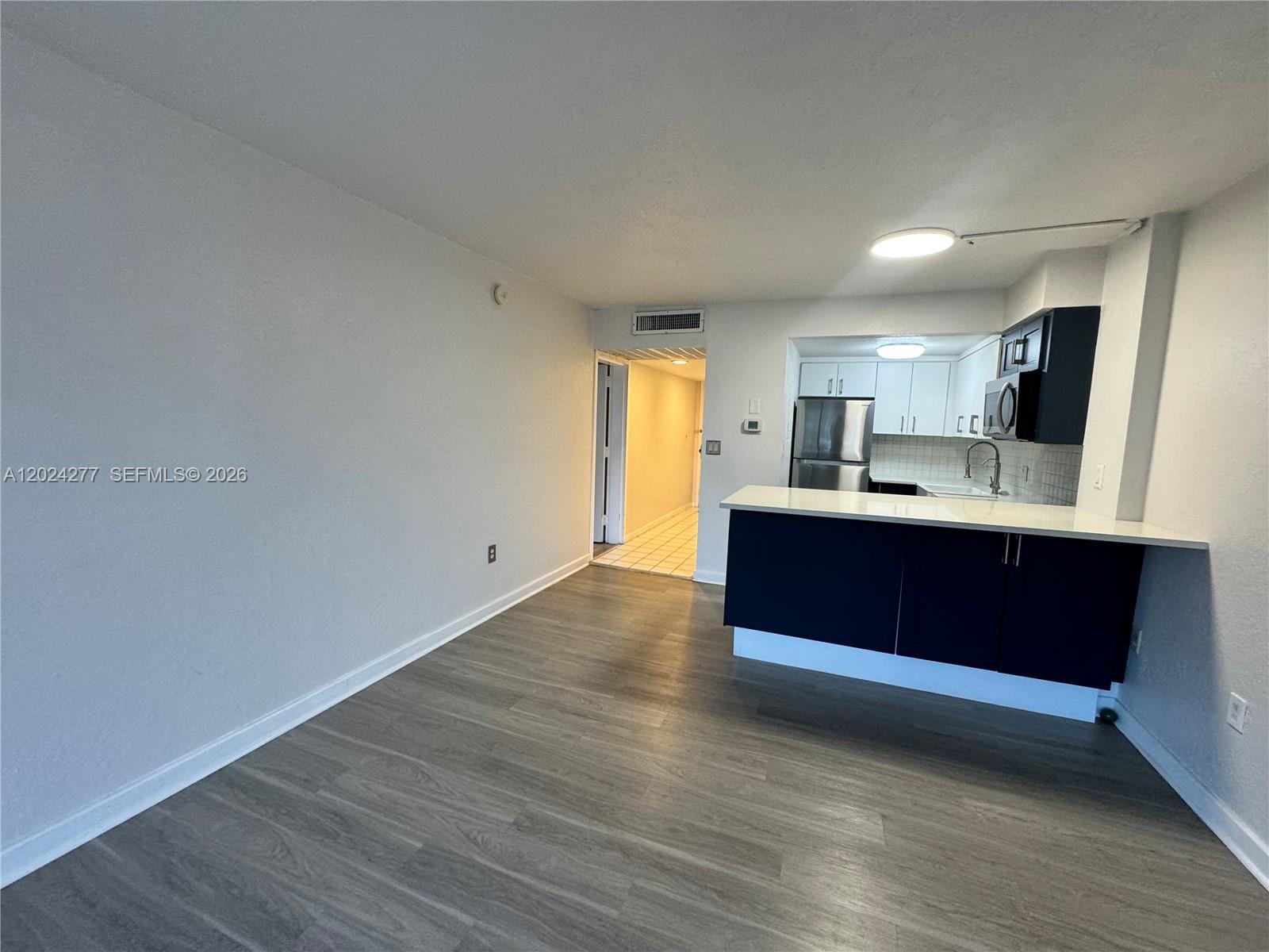 A kitchen with dark cabinets and a breakfast bar opens into a living area — 1650 NE 115th St # 609, Miami FL 33181, MIAMI, FL