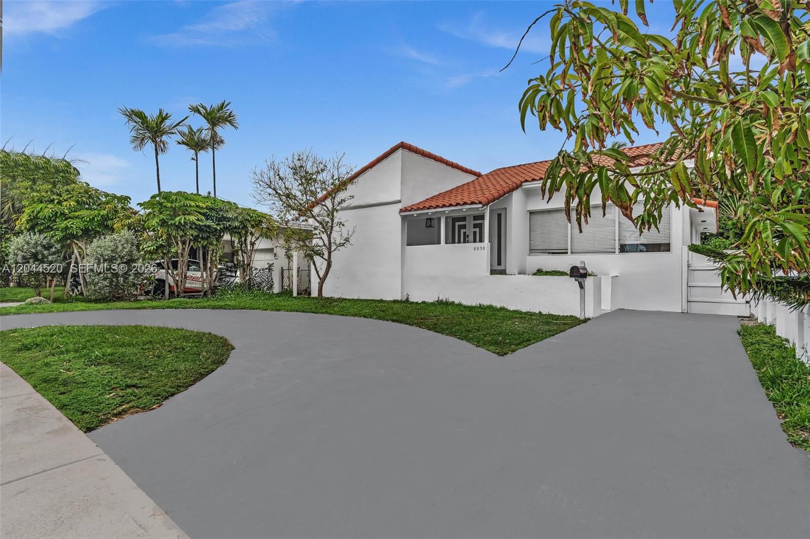 A white house with a red tile roof features a curved gray driveway and landscaping — 8858 Harding Ave, Surfside FL 33154, SURFSIDE, FL