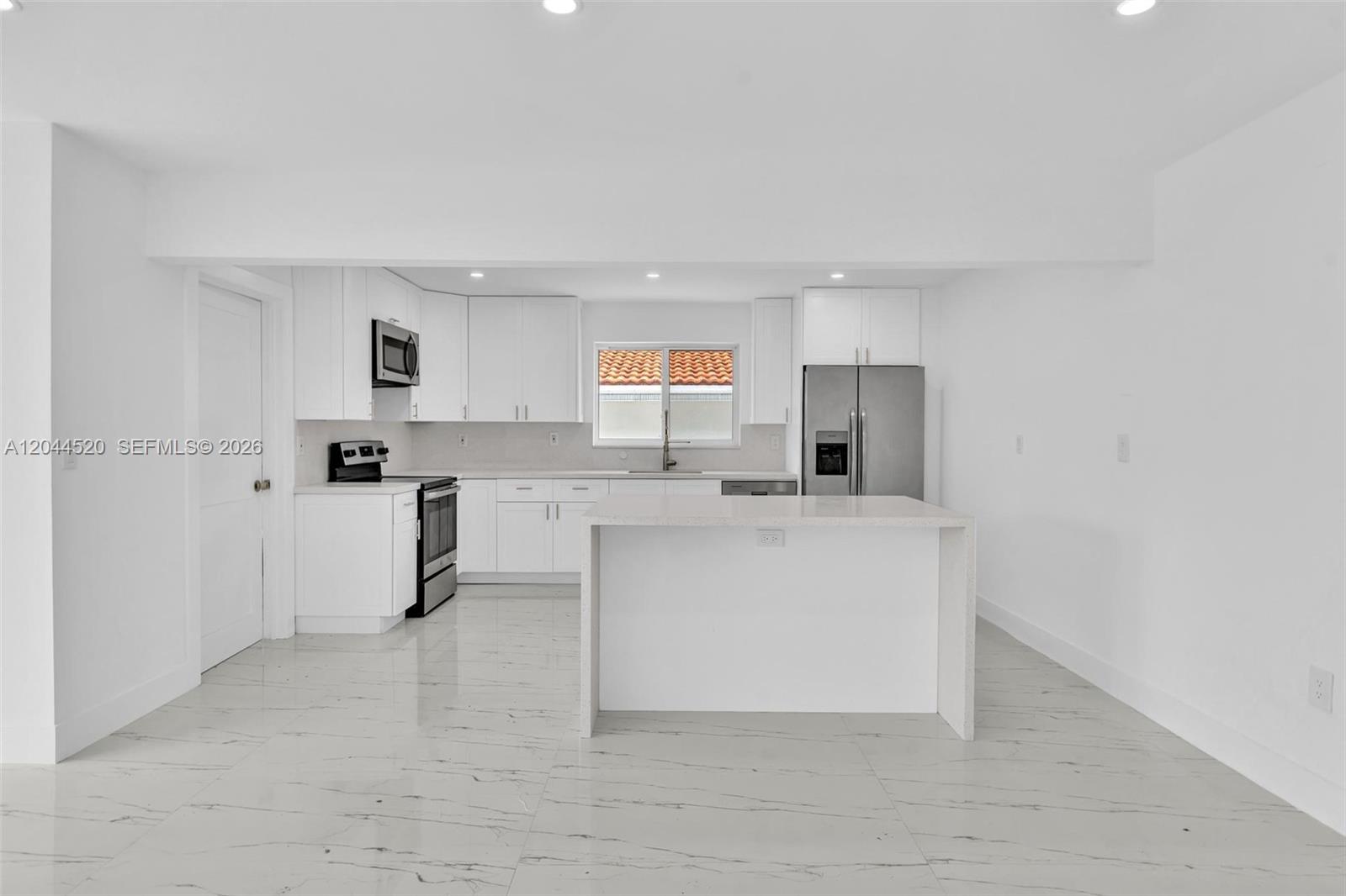 A modern white kitchen features a central island, stainless steel appliances, and marble-look tile flooring — 8858 Harding Ave, Surfside FL 33154, SURFSIDE, FL