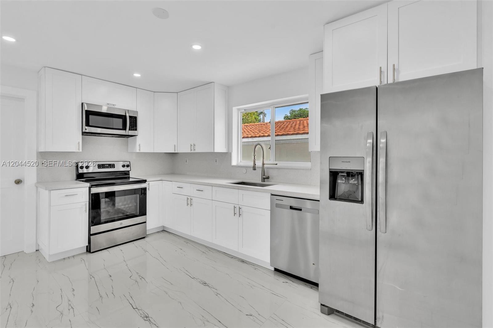 A modern kitchen features white cabinets, stainless steel appliances, and white marble-patterned tile flooring — 8858 Harding Ave, Surfside FL 33154, SURFSIDE, FL