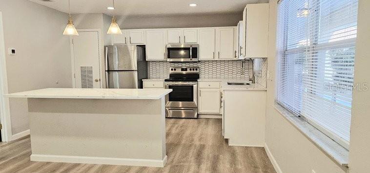 A kitchen features white cabinets, stainless steel appliances, a marble-topped island, and light wood flooring — 4387 JACKSON STREET UNIT J-E, PORT CHARLOTTE, FL