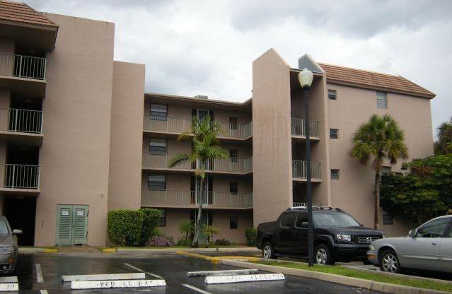 A multi-story apartment building with beige stucco walls, balconies, and a parking lot in front — 3100 N Pine Island Road # 202, Sunrise FL 33351, SUNRISE, FL