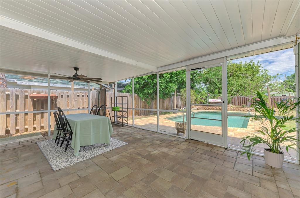 A screened-in patio with stone flooring overlooks a backyard swimming pool and wooden fence — 71 WINSON AVENUE, ENGLEWOOD, FL