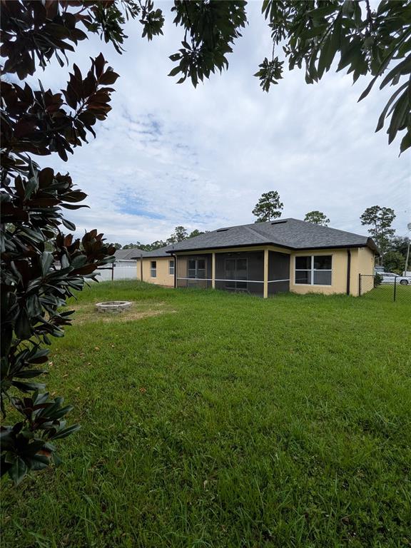 The backyard of a single-story house features a screened-in porch and a stone fire pit — 43 RAEMOOR DRIVE, PALM COAST, FL