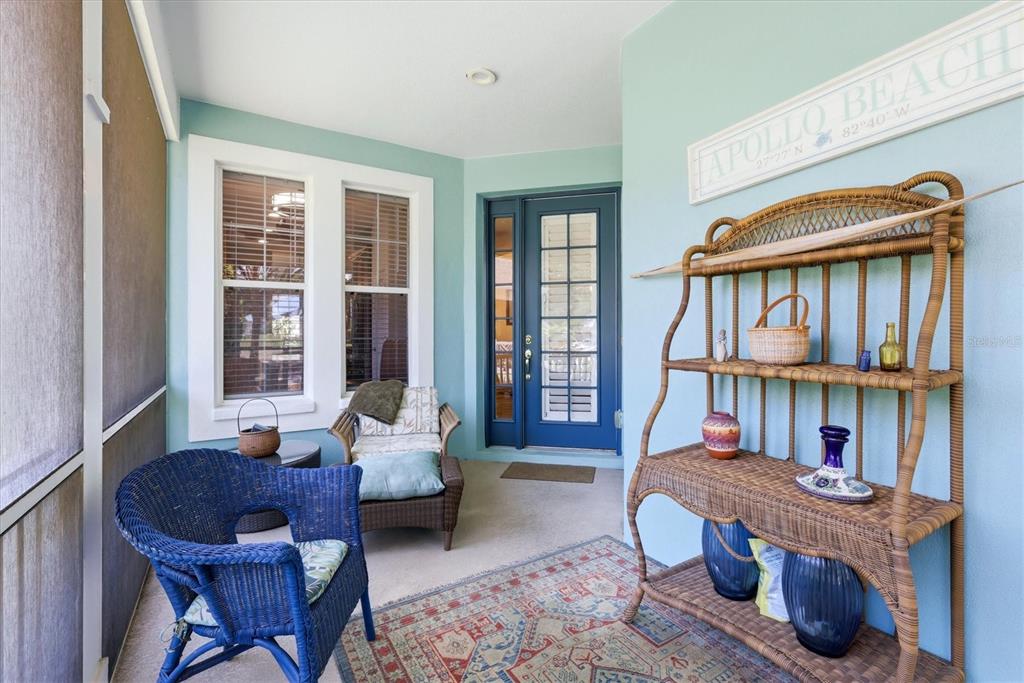 A covered porch features a blue wicker chair, a wicker shelving unit, and a blue door — 5318 GOLDEN ISLES DRIVE, APOLLO BEACH, FL