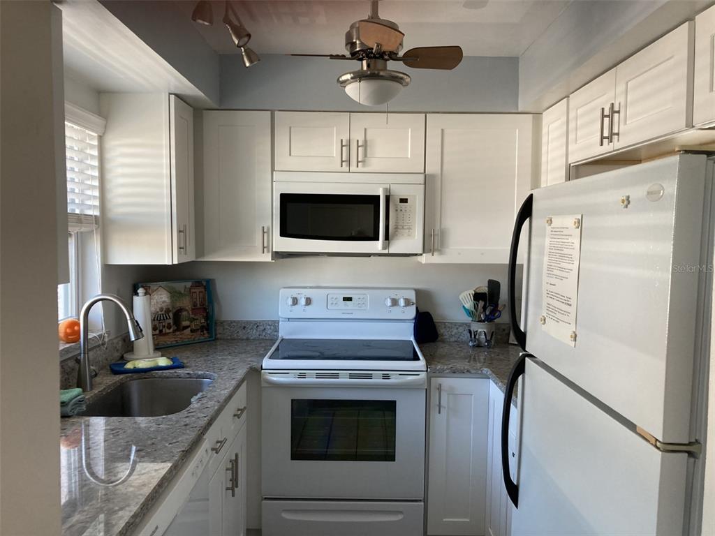 A kitchen features white cabinets, granite countertops, and white appliances — 304 47TH AVENUE DRIVE W UNIT 307, BRADENTON, FL